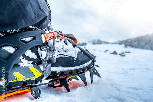 Foot with crampon on boot standing on winter mountain snow photo