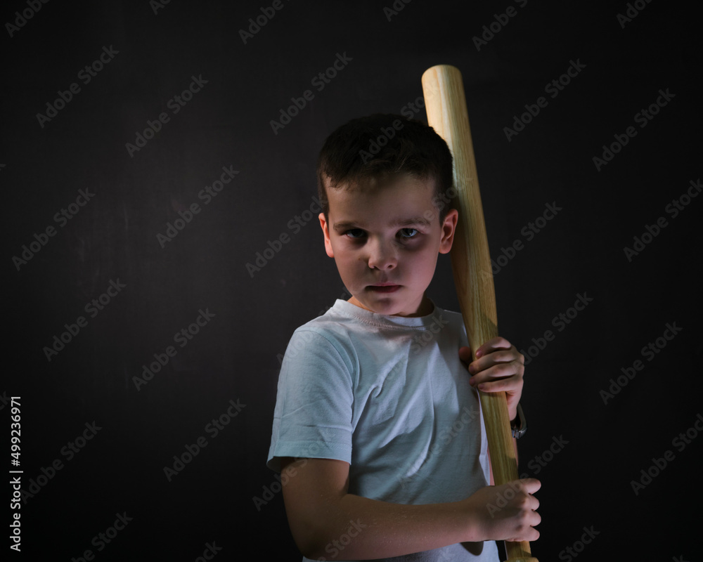 Angry boy on a black background with a bat in his hand.The European has a serious look.looks at the camera angry Angry boy on a black background with a bat in his hand.The European has a serious look.looks at the camera angry