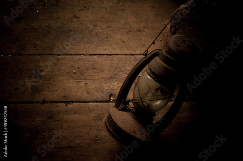 Amazing vintage kerosene lamp on a shabby wooden floor. Extremely dark background, brown color