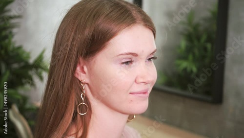redhead model sits and smiles while makeup artist applies foundation to her face