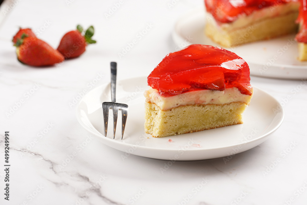 a Piece of a three-layered cake with vanilla pudding, strawberry jelly and fresh strawberries on a white marble background