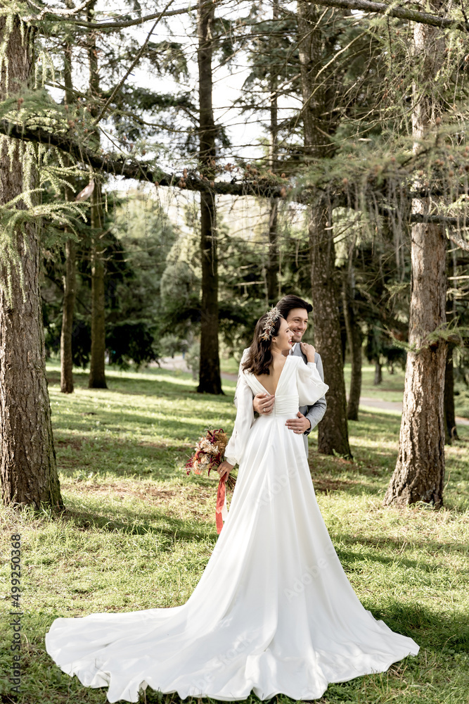 The groom hugs a beautiful bride in a white long wedding dress in the forest The groom hugs a beautiful bride in a white long wedding dress in the forest