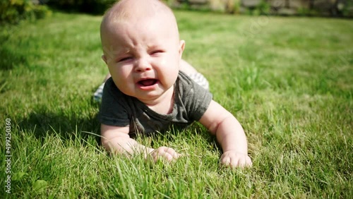 two-month-old baby lies on lawn and cries