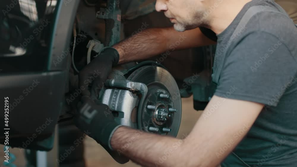 Selective focus disc brake on car, Car brake repairing in garage. Portrait Shot of a Mechanic Working on a Vehicle in a Car Service. Modern Clean Workshop. Car service, maintenance and people concept
