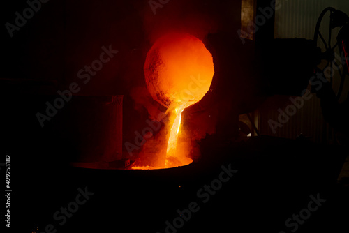 The work of the foundry. Pouring hot metal from the bucket into molds. Bright red metal, smoke and sparks flying to the sides