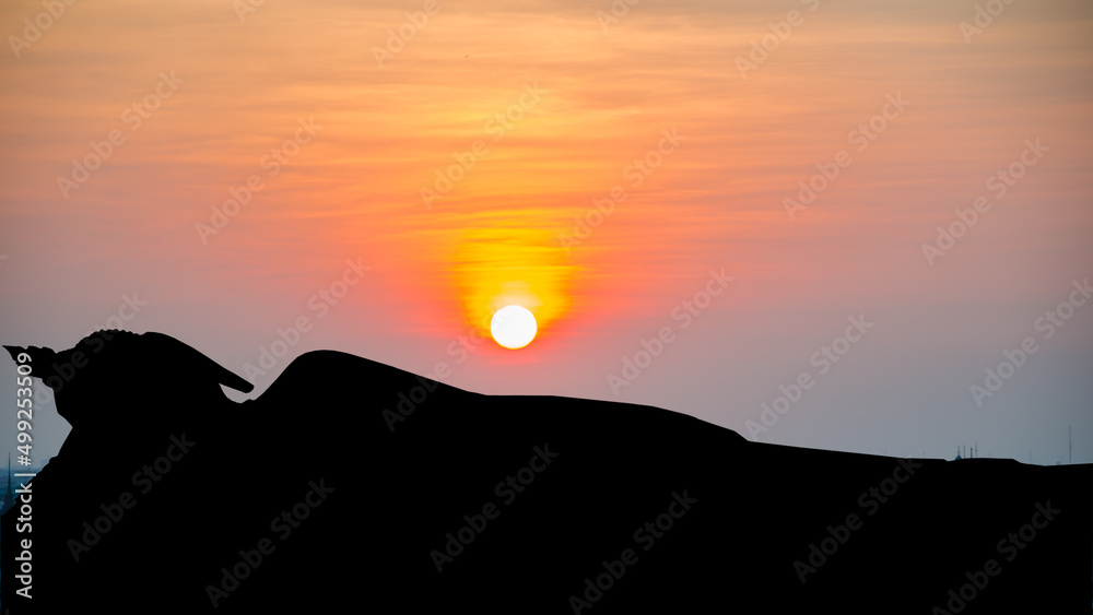 Silhouette reclining buddha on sunset background.