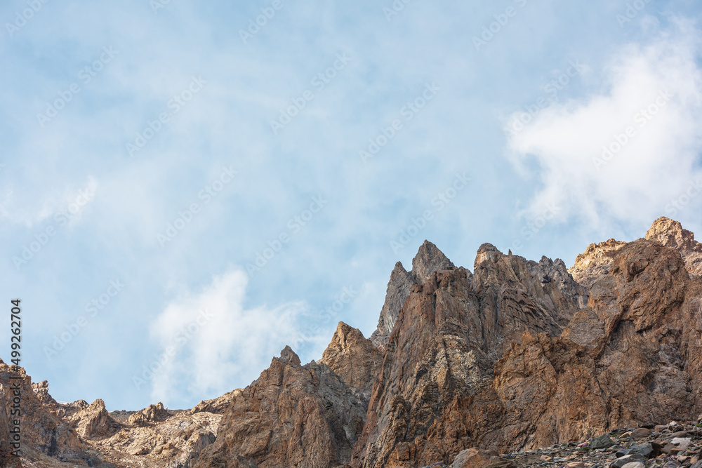 Scenic alpine landscape with sunlit rocky mountains in cloudy sky. Colorful mountain scenery with sharp rocks in sunlight under cirrus clouds. Awesome view to high rockies in sunshine in cloudiness.