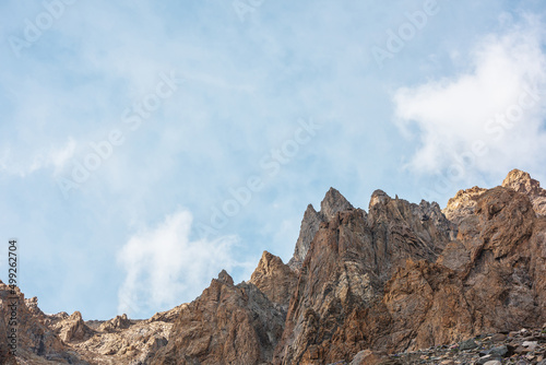 Scenic alpine landscape with sunlit rocky mountains in cloudy sky. Colorful mountain scenery with sharp rocks in sunlight under cirrus clouds. Awesome view to high rockies in sunshine in cloudiness. © Daniil