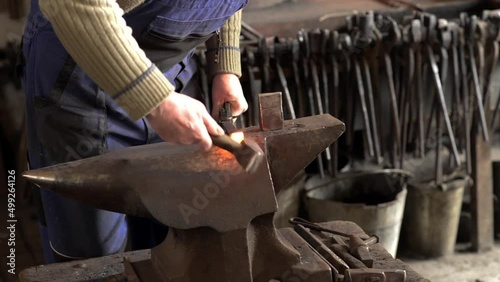 Blacksmith forges hinge on a anvil. Hammering hot red steel