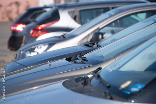 Many cars parked next to each other in a row in a parking lot. Focus on the wipers, nozzles and windshield of the second car
