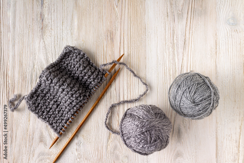 Fototapeta premium knitted fabric on wooden knitting needles and balls of yarn on a white wooden background