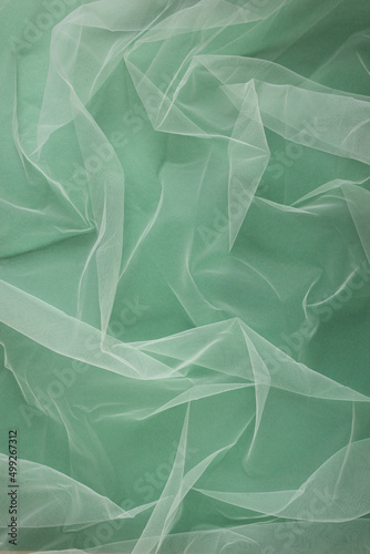 Fotografía transparent tulle fabric arranged in soft folds on a green background, selective