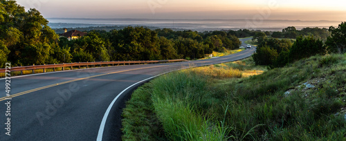S shape curved road winding through a hilly terrain with a guard rail and a vehicle and hills in the distance, Guadalupe Valley, Texas photo