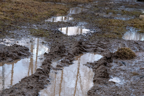 dark brown path with muddy pits and large puddles. Dirt road in village. Difficulties of traveling on country road during rainy season