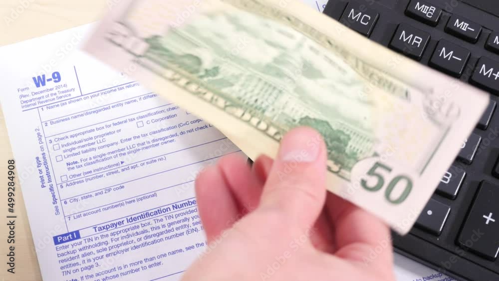 Men's hands throw several hundred dollar bills on the table with a calculator and a W-9 tax form. Tax payment, personal accounting, financial planning. Men's hands throw several hundred dollar bills on the table with a calculator and a W-9 tax form. Tax payment, personal accounting, financial planning.