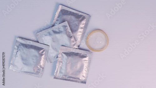 Woman's finger picks up a condom among several silver packages and puts AIDS awareness red ribbon.
