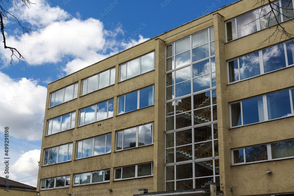 Sky and clouds reflected in yellow concrete building windows with visible staircase Sky and clouds reflected in yellow concrete building windows with visible staircase