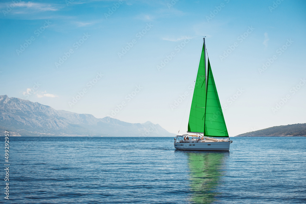 White yacht with green sails in the sea against a background of blue sky and mountains