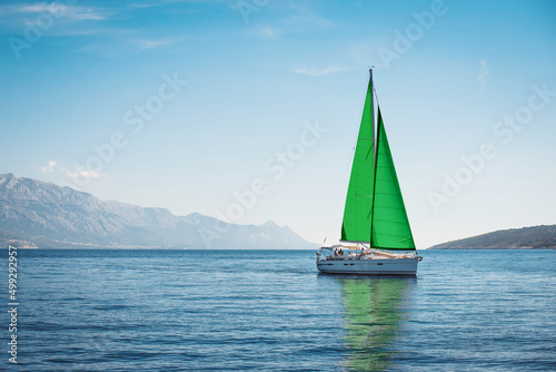 White yacht with green sails in the sea against a background of blue sky and mountains © Maxim Sokolov