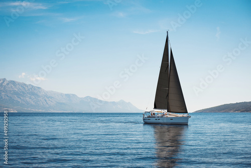White yacht with black sails in the sea against a background of blue sky and mountains © Maxim Sokolov
