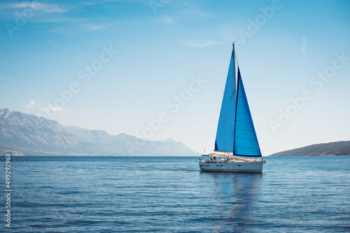 White yacht with blue sails in the sea against a background of blue sky and mountains © Maxim Sokolov