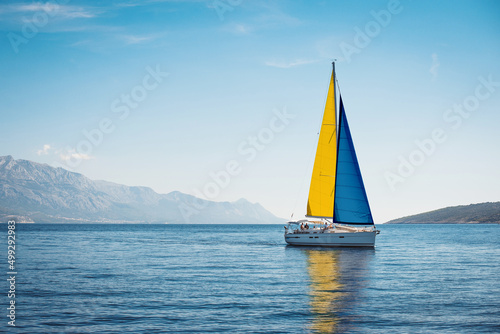 A white yacht with Swedish flag sails at sea against a background of blue sky and mountains © Maxim Sokolov