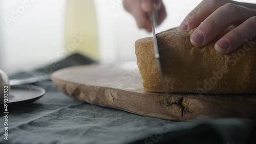 Man slicing ciabatta with bread knife on olive board photo