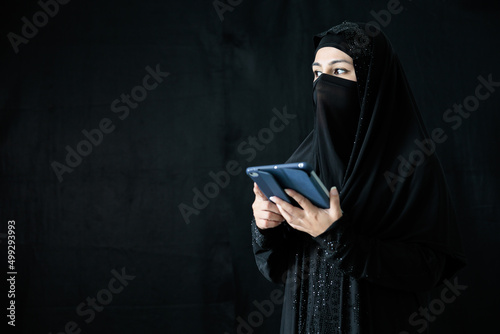 mysterious muslim woman using tablet computer on black background