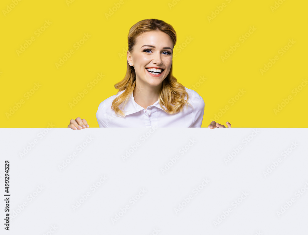 Very happy excited, laughing business woman in white confident clothing standing behind empty banner signboard with copy space text area. Success and advertising concept. Yellow background. Very happy excited, laughing business woman in white confident clothing standing behind empty banner signboard with copy space text area. Success and advertising concept. Yellow background.