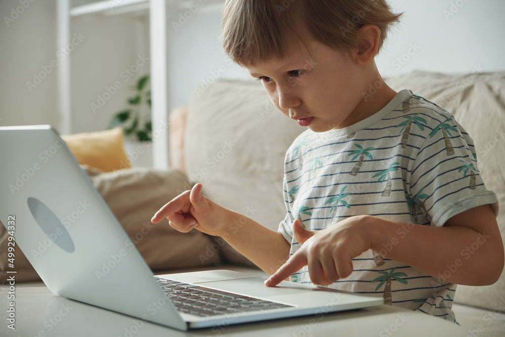 Happy child typing using laptop sitting on sofa at home, Homeschooling, remote education Happy child typing using laptop sitting on sofa at home, Homeschooling, remote education