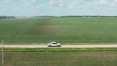 Aerial side view, white pickup truck driving on rural countryside unpaved farm road photo