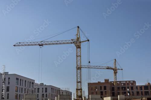 Two tower cranes near high rise building with concrete building under construction.