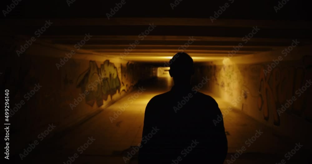 Silhouette of the back of a man walking in a dark underpass. Dark scary ...