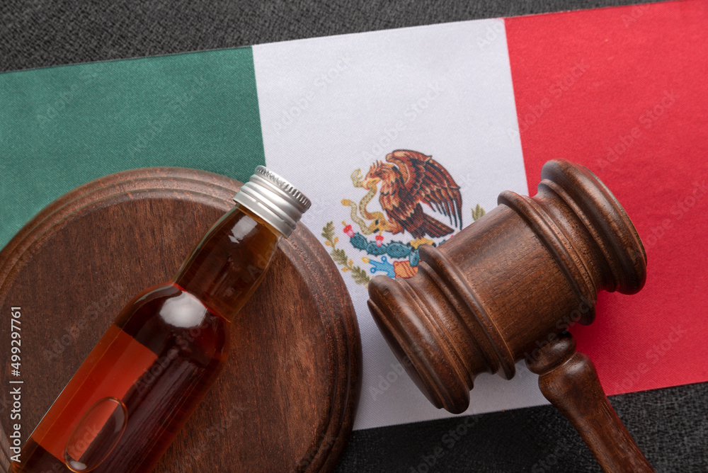 Alcohol bottle and wooden gavel on Mexico flag background. Concept alcohol and conflicts with the law in Mexico .