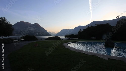 Sunrise on Lake Lugano seen from a garden with a fountain, Ticino, Switzerland. Popular travel destination