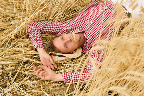 Happy male farmer laying on barley stalks and relaxing at barley meadow. Young agronomist lying on wheat stems and resting at cereal field. Concept of agricultural business.