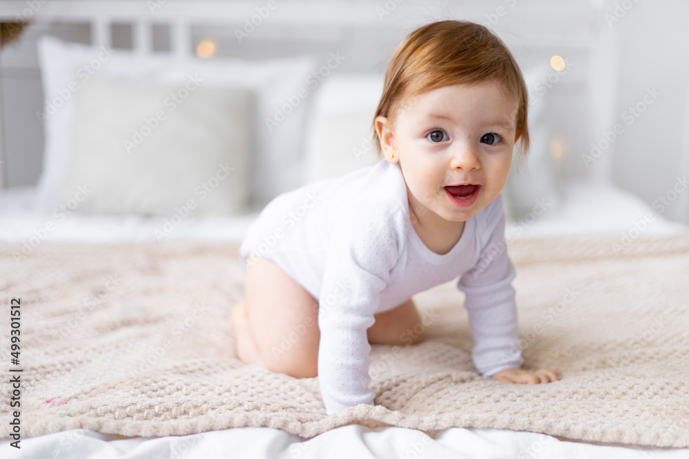a small child girl learns to crawl on a bed in a bright room on cotton white linen, close-up portrait a small child girl learns to crawl on a bed in a bright room on cotton white linen, close-up portrait