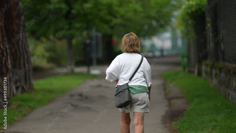 Back of older woman walking outside in urban path