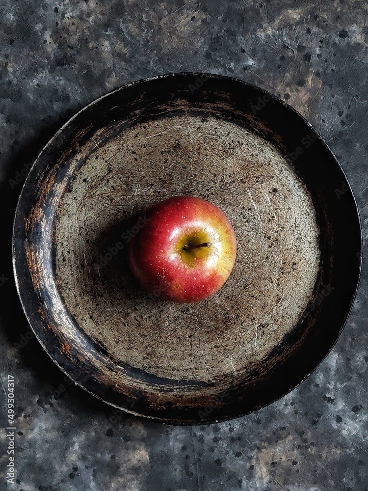 Red apple in the center of retro plate on black concrete background. Flatlay with summer fruit and water drops. Red delicious.