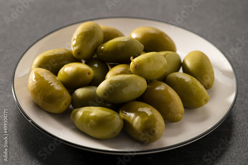 Green pickled olives on a dark gray background, square format, close-up