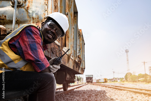 Portrait of Africa American man engineering holding railing and with wear hardhat in front of train station. Preparation for train mechanical operation. Technician man