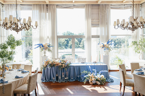 Blue wedding decor. Festive table decorated with flowers on the center, candles, silverware and plates with silk napkins on dusty blue tablecloth