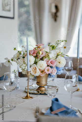 Blue wedding decor. Festive table decorated with flowers on the center, candles, silverware and plates with silk napkins on dusty blue tablecloth