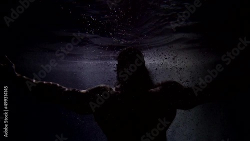 dark silhouette of Poseidon in depth of ocean, brawny man with muscular hands and torso underwater
