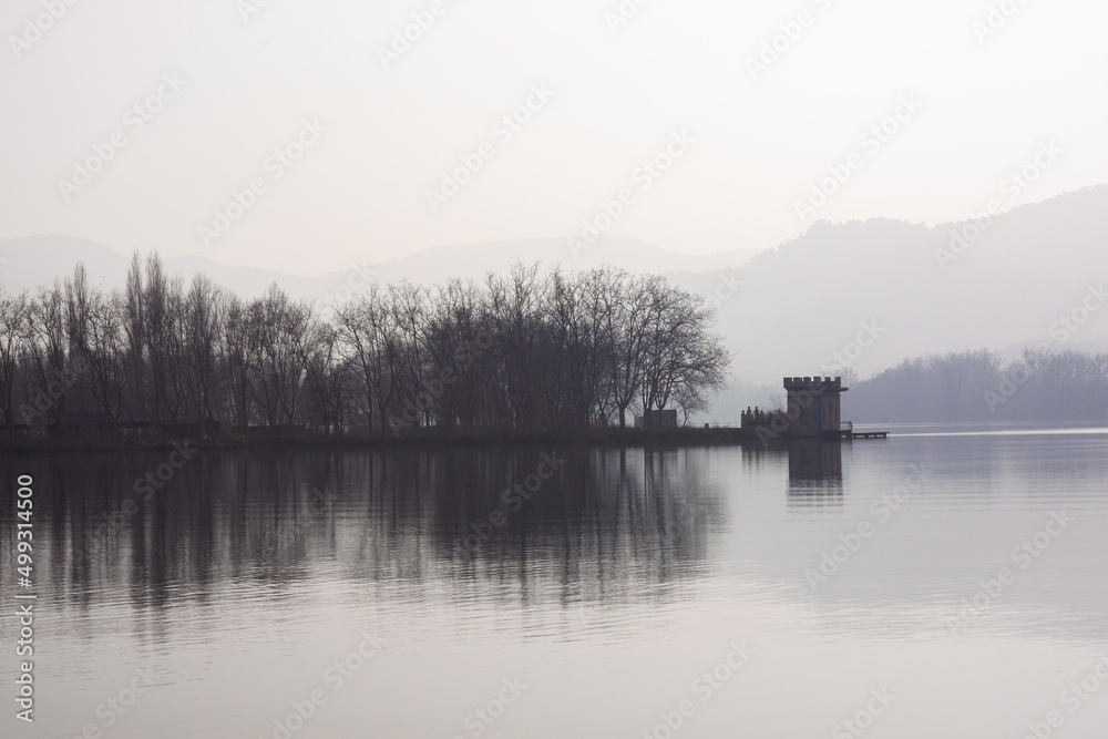 Fog over the lake with silhouette of mountains in the background.