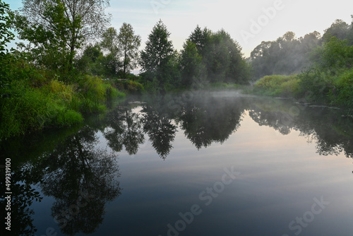 The river is covered with morning fog at sunrise  surrounded by a dense green forest. Wild nature. Active weekend vacations wild nature outdoor.