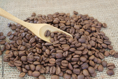 Roasted coffee beans in wooden scoop on brown burlap or sack cloth background.