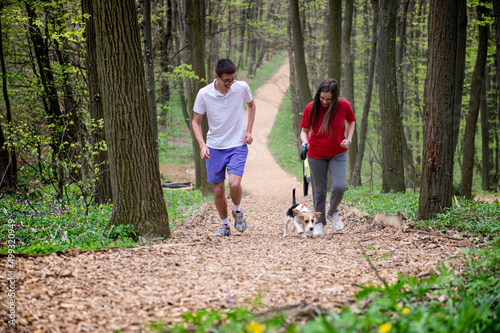 A young girl and a boy runs through the forest with their dog