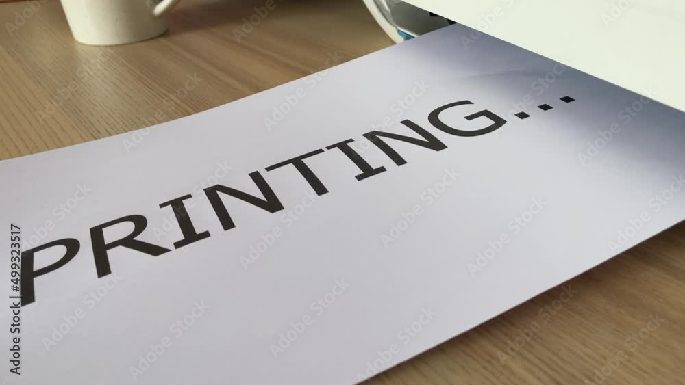 Printing “PRINTING” text written message word on paper sheet document. Close up A4 page being printed from multifunction scanner printer on wooden desk in office. Hand take paper from printer