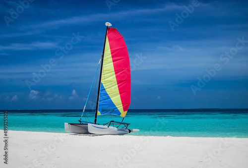 Sailing boat with colorful sail on sandy beach near the ocean bay. Travel tourism concept.